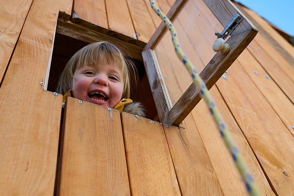 Kind schaut aus Spielhaus und lacht.